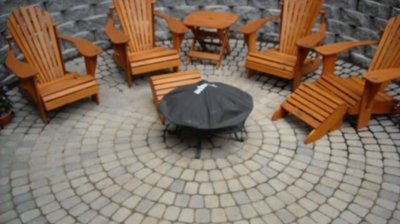 A stone patio with a fire pit and wooden furniture Photo