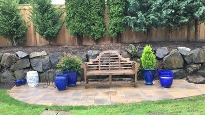 A wooden bench on a stone patio with grass and a stone wall behind it Photo